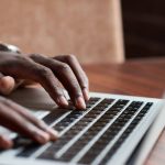 Close-up of unrecognizable businessman typing on laptop editing online document at table